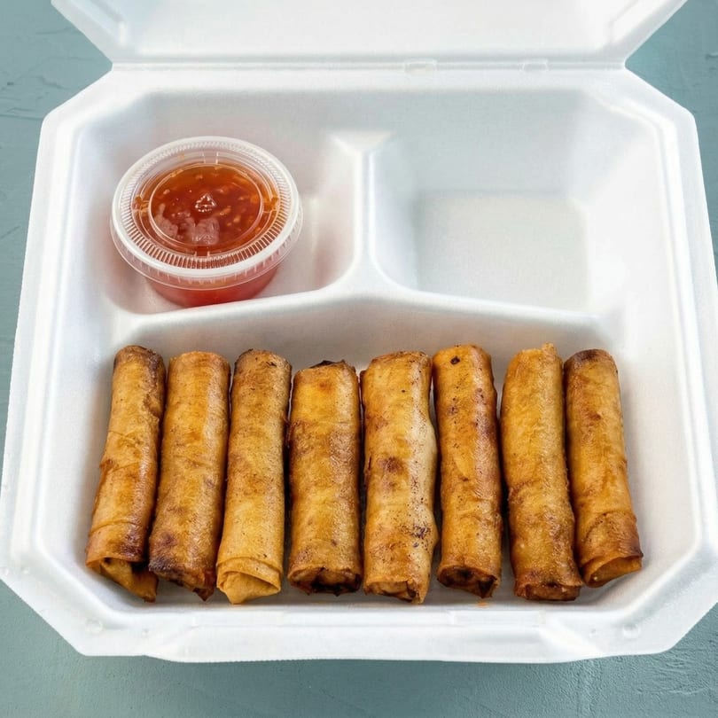 Eight crispy egg rolls and a small container of sweet chili sauce in a white takeout box.