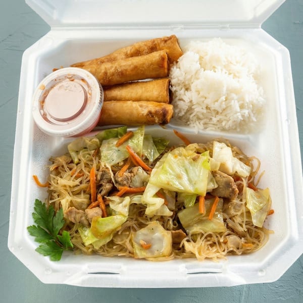 A takeout container with pancit, rice, four lumpia, and a small cup of sauce.